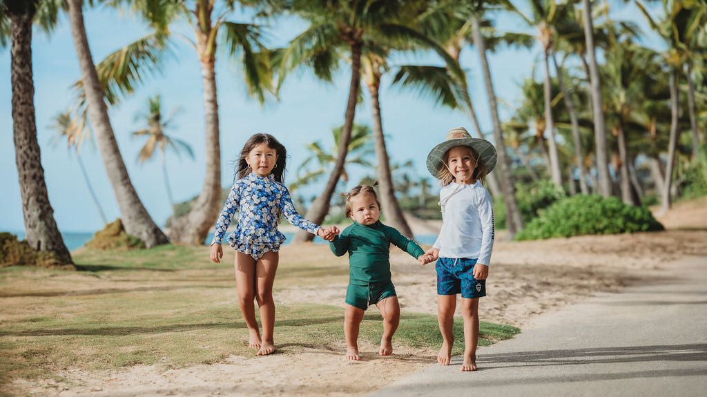 Kids wearing straw lifeguard hats in baby, toddler, and youth sizes playing together on the beach.