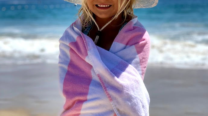 Girl wearing straw lifeguard hat wrapped in striped towel by the beach or pool