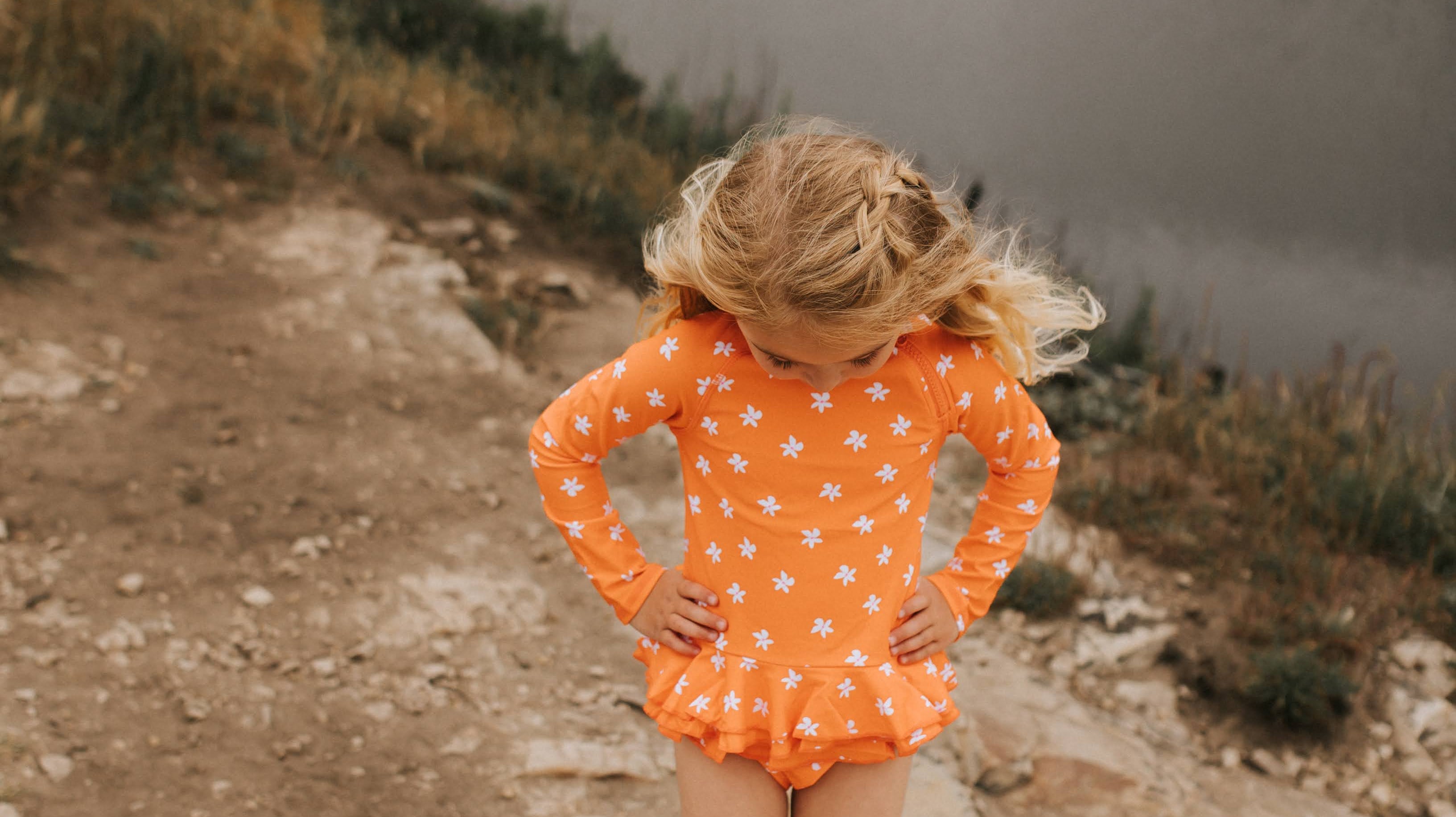 Girl in Plumeria Orange Two Piece Ruffle Set standing by a pool of water, clearly visible in the bright color