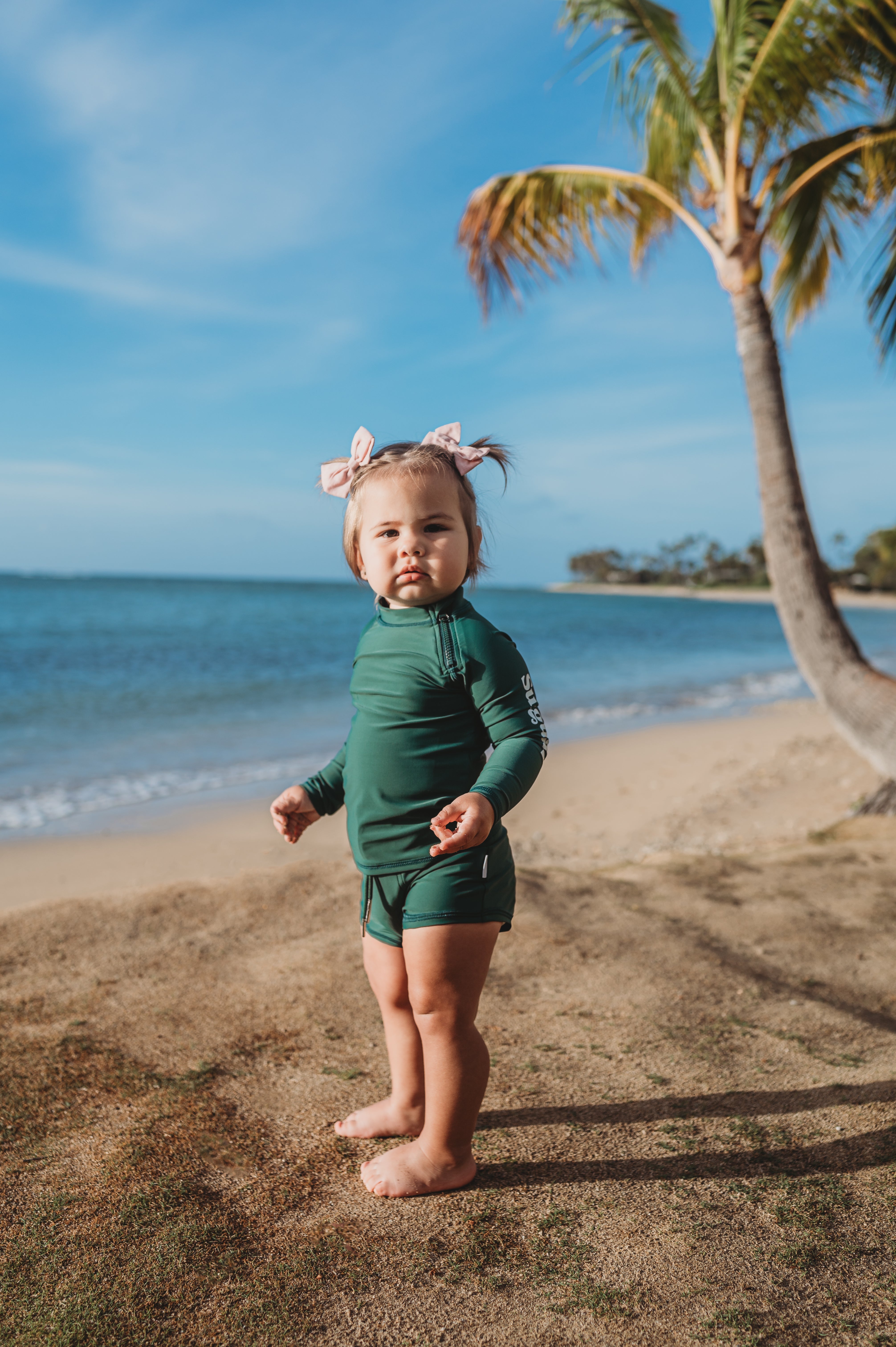 Smiling baby wearing a UPF 50+ sunsuit and sun hat playing on the beach