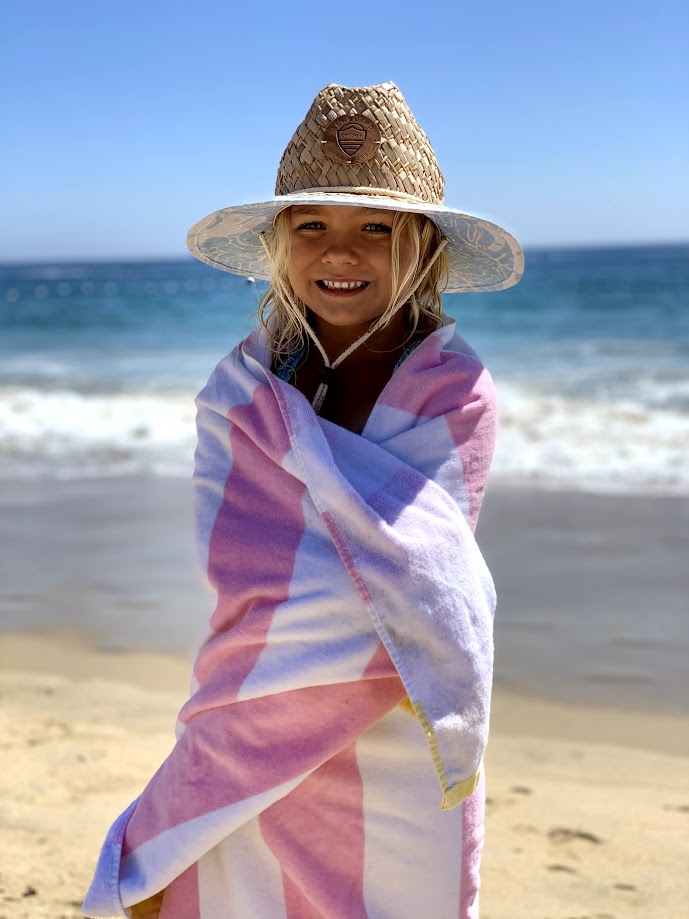 Girl wearing straw lifeguard hat wrapped in striped towel by the beach or pool