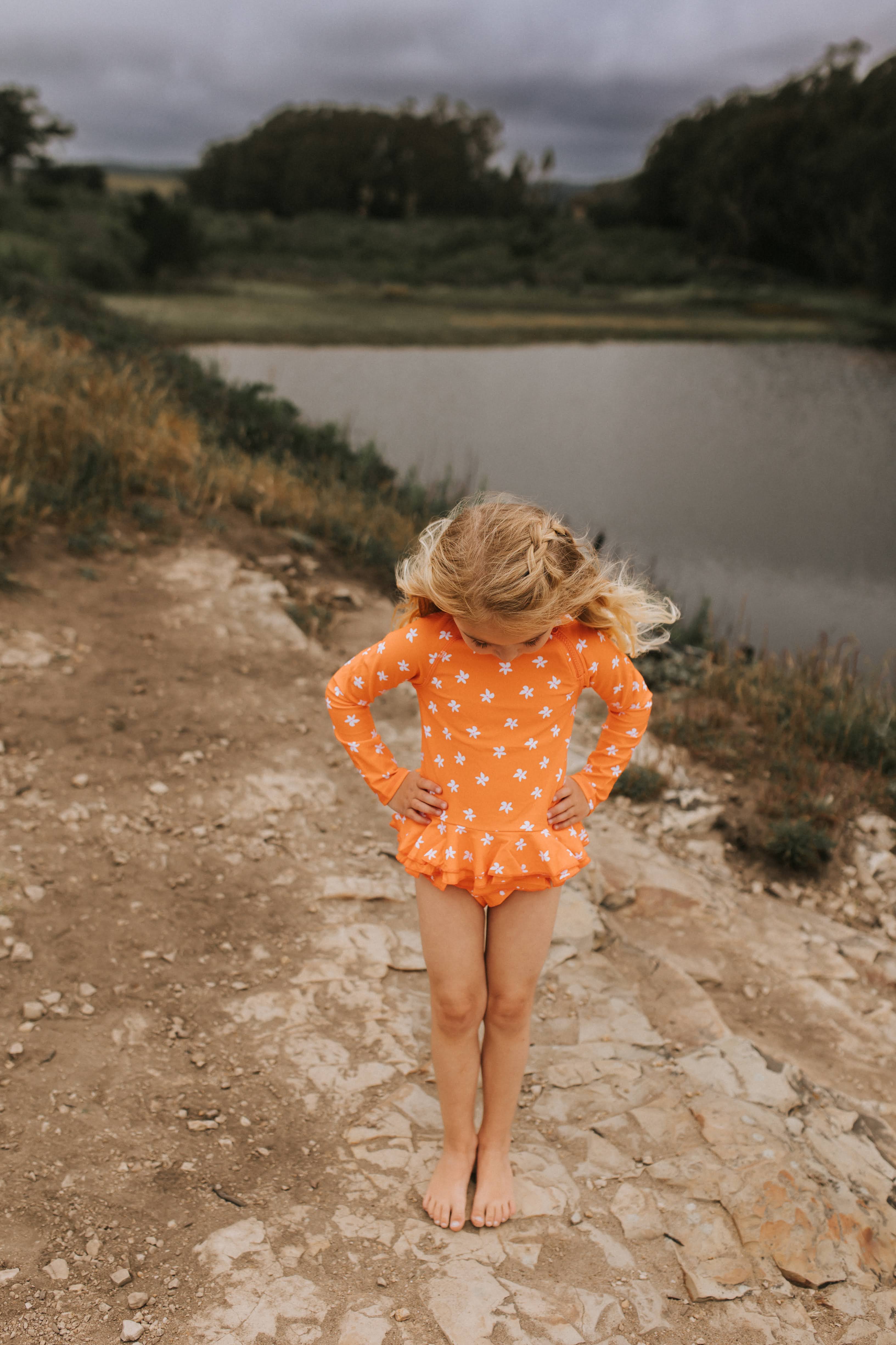 Girl in Plumeria Orange Two Piece Ruffle Set standing by a pool of water, clearly visible in the bright color