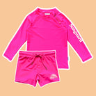 Pink long-sleeve rash guard and shorts set with 'Suneguard' branding on a beige background
